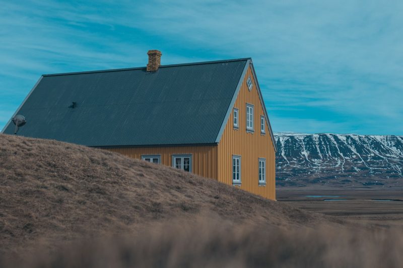 Charming yellow house with a corrugated roof set against a scenic Nordic countryside backdrop.