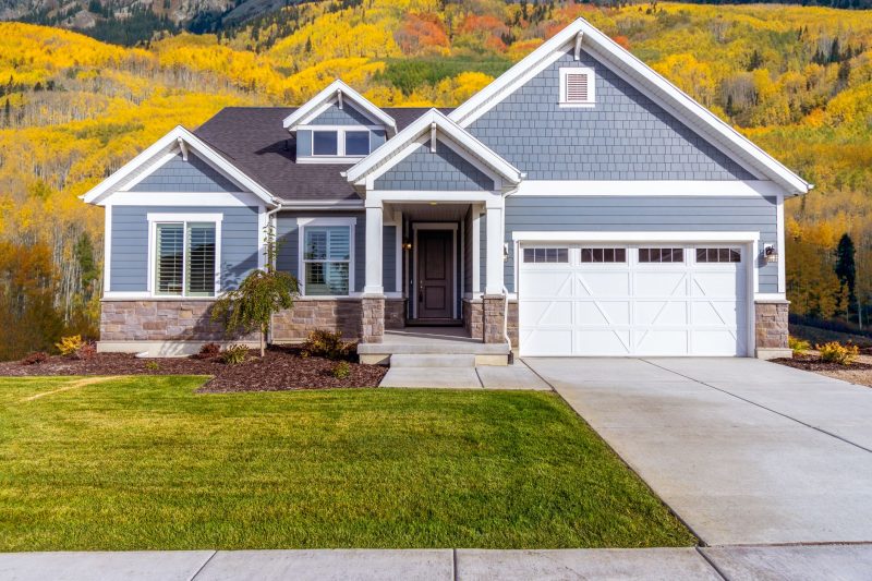 Suburban house surrounded by colorful autumn trees and leaves in a bright, sunny setting.